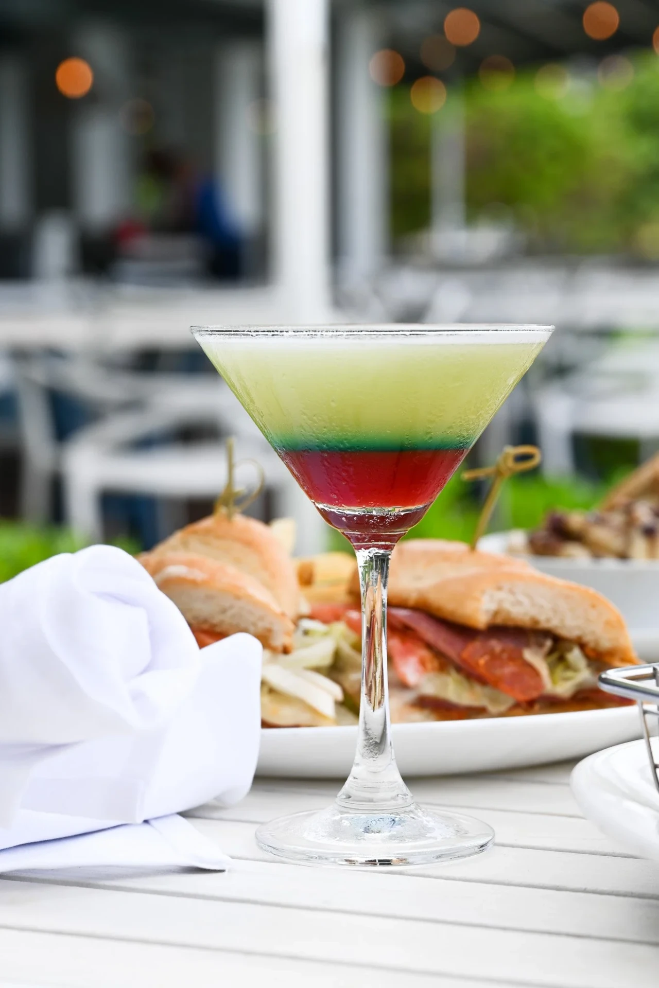 Layered green and red martini beside an Italian sandwich on a lanai table