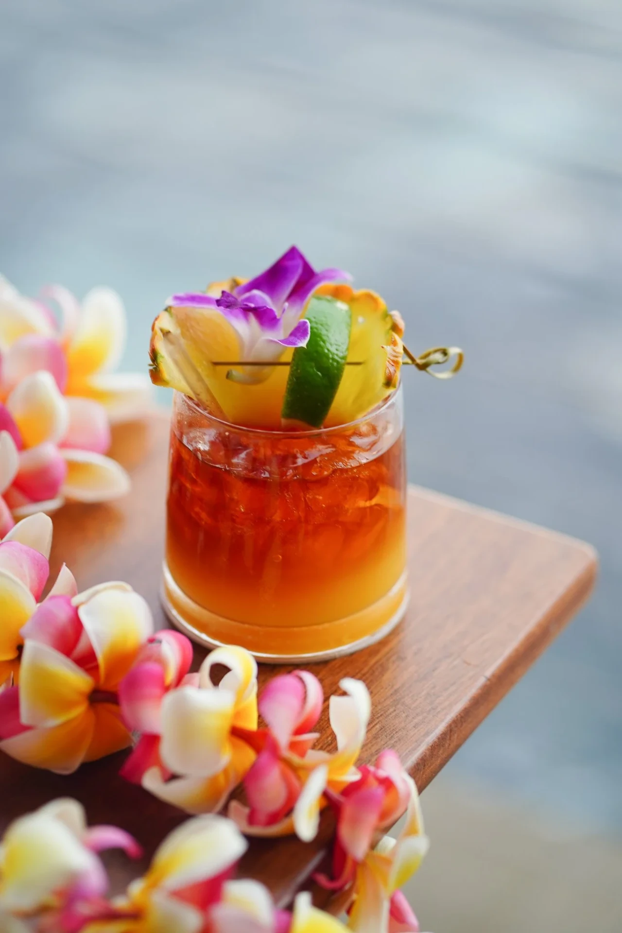 Mai tai garnished with pineapple, lime and orchid beside a plumeria lei