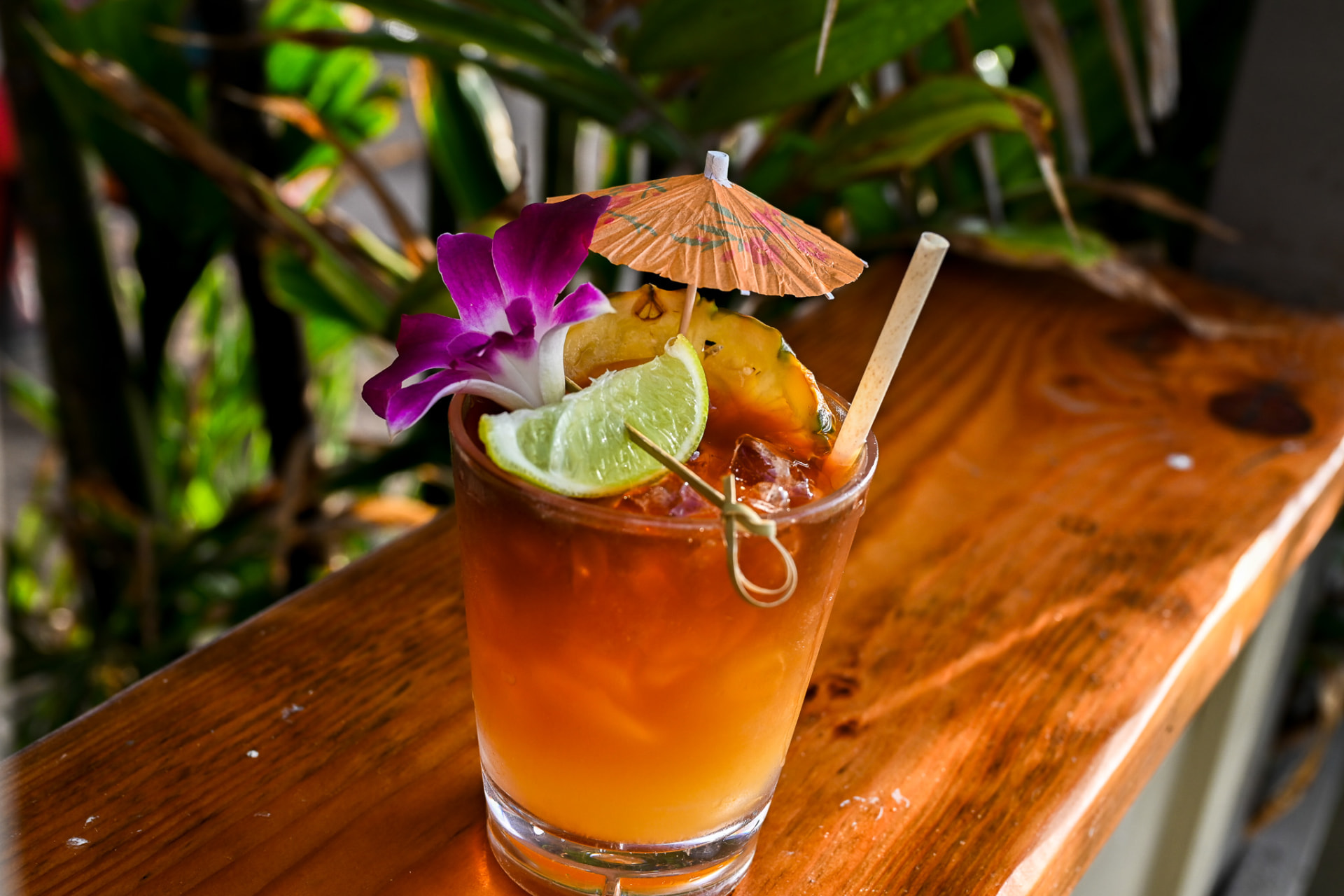 Mai tai with pineapple, lime and a purple orchid on a koa wood rail