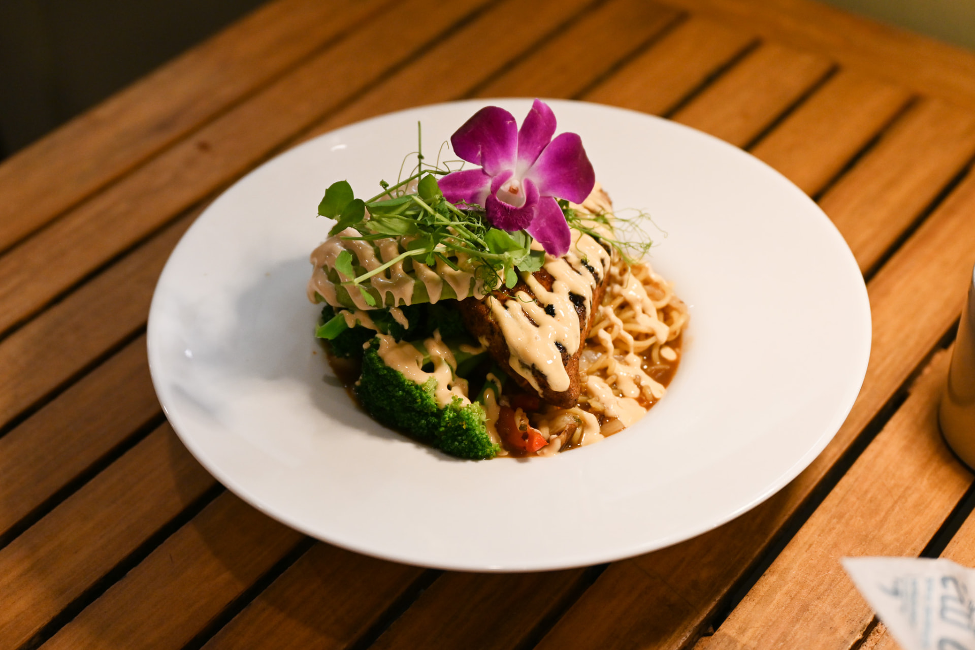 Seared fish over crispy noodles with broccoli, creamy sauce and an orchid