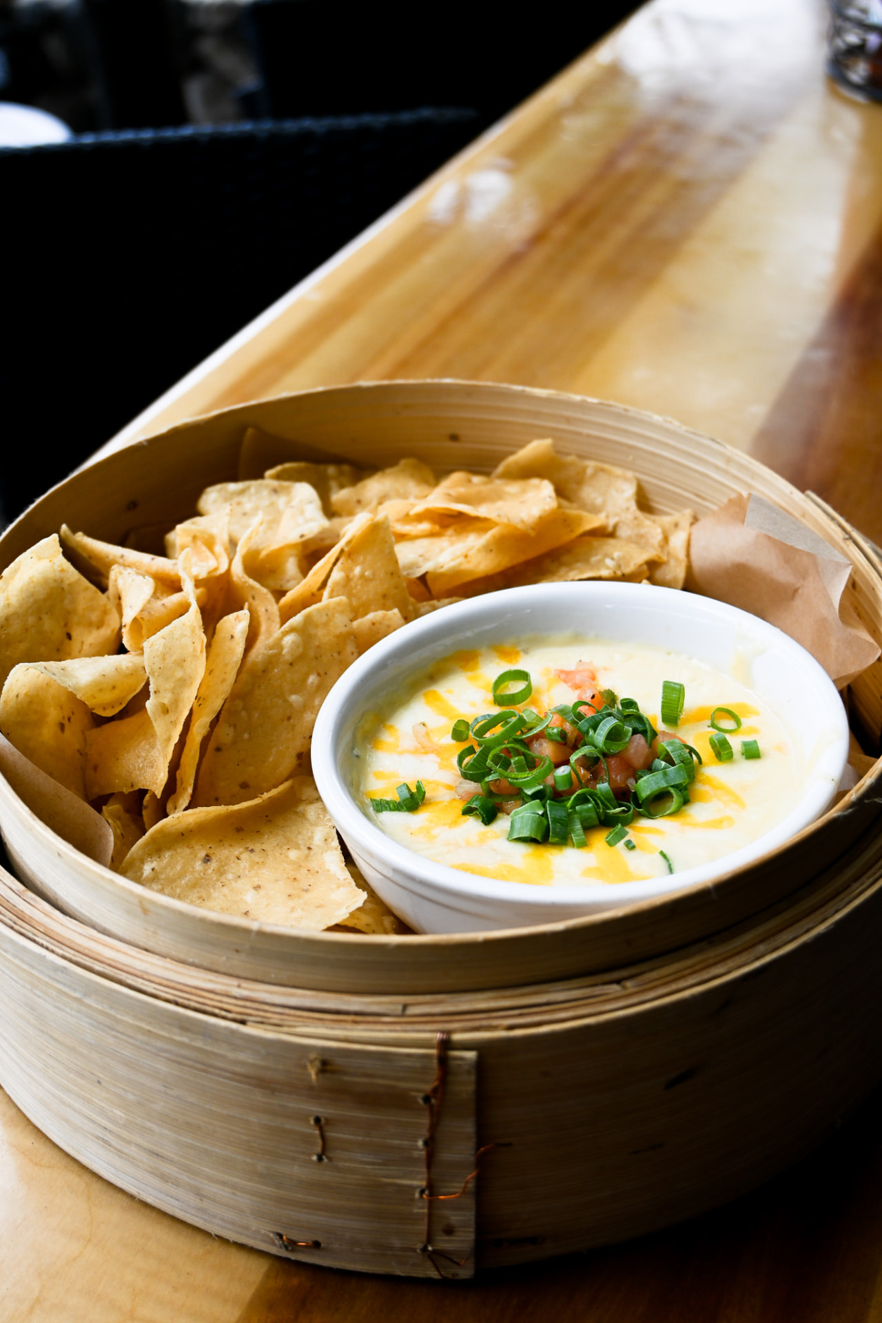 Warm queso topped with pico and green onion served with tortilla chips in a bamboo steamer